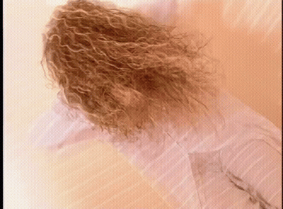 Curly Hair Woman Laying On Bed In White Shirt GIF