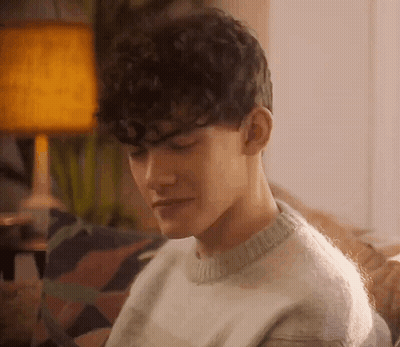 Curly-Haired Man In Sweater On Couch GIF