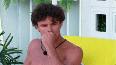 Curly-Haired Shirtless Man Covering Nose On Yellow Couch GIF