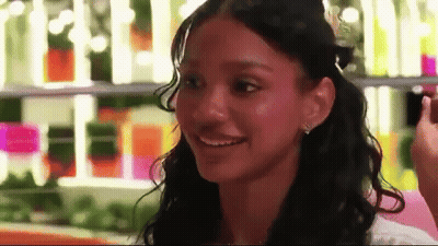 Curly-Haired Woman Smiling At Bottle Shelf GIF