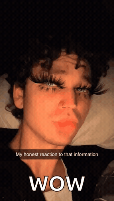 Curly-Haired Young Man With Fake Eyelashes On Bed Says Wow GIF