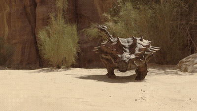 Dinosaur Standing In Sand Near Rock GIF