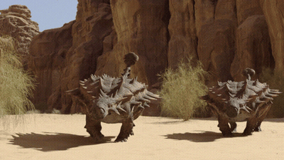 Dinosaurs Walking In Desert Near Rocks GIF