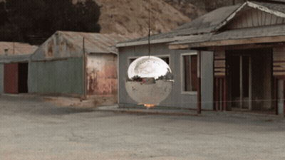 Disco Ball Hanging From Rope In Front Of Buildings GIF