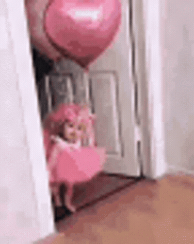 Doll In Pink Dress Next To Pink Heart Balloon In Doorway GIF