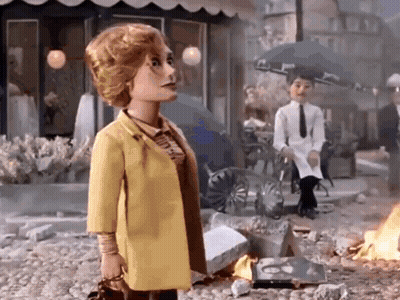 Doll In Yellow Coat In Front Of Burning Building GIF
