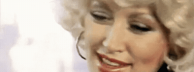 Dolly Parton Is Wearing A Blonde Wig And Hoop Earrings While Smiling . GIF