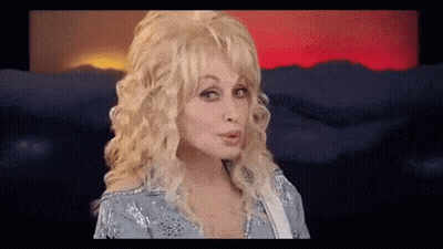 Dolly Parton Making Funny Face Holding Guitar In Front Of Mountains GIF