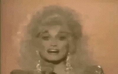 Dolly Parton Singing Into Microphone In Front Of Pink Wall GIF
