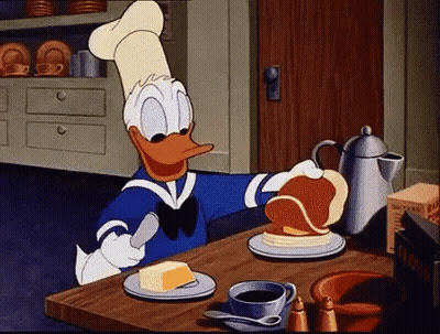 Donald Duck Is Spreading Butter On A Pancake At A Table . GIF