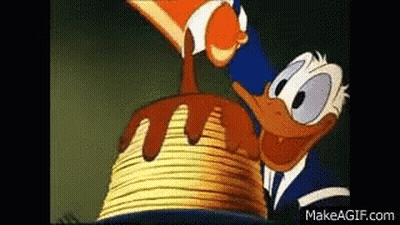 Donald Duck Is Standing Next To A Stack Of Pancakes With Chocolate Sauce Being Poured On Them . GIF