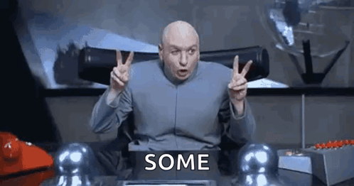 Dr. Evil From The Movie Dumb And Dumber Is Sitting At A Desk Giving A Peace Sign . GIF