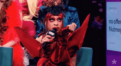 Drag Queen Holding Microphone In Front Of Nutmeg Sign GIF