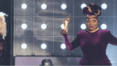 Drag Queen In Purple Dress Holding High Heels GIF