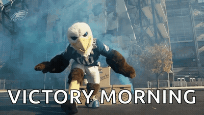 Eagle Mascot Says Victory Morning In Front Of Large Building GIF