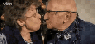 Elderly Couple Kissing In Front Of Christmas Tree GIF