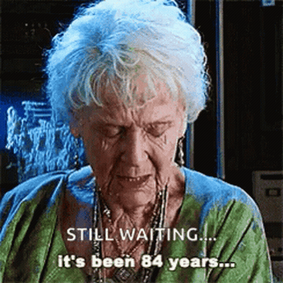 Elderly Woman Gray Hair Green Shirt Says Still Waiting It's Been 84 Years GIF