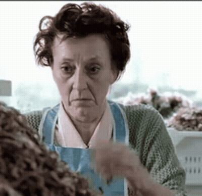 Elderly Woman in Blue Apron Standing at Counter