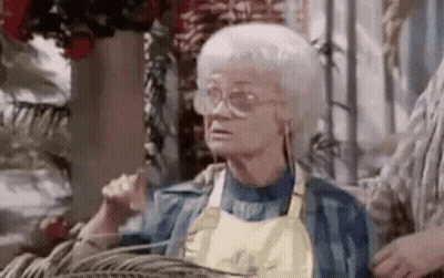 Elderly Woman in Glasses and Apron Sitting