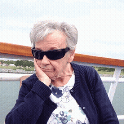 Elderly Woman In Sunglasses And Blue Sweater Touching Face GIF