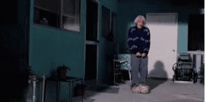 Elderly Woman Standing In Front Of Blue House GIF