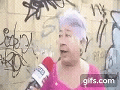 Elderly Woman Talking Into Microphone In Front Of Graffiti Wall GIF