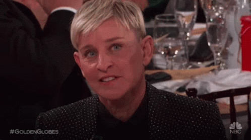 Ellen Degeneres Is Sitting At A Table With Wine Glasses And Making A Funny Face . GIF