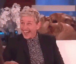 Ellen Degeneres Is Smiling While Sitting On A Couch In Front Of A Statue . GIF