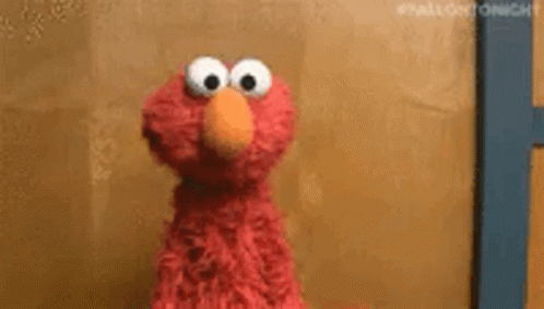 Elmo From Sesame Street Is Looking At The Camera While Standing In Front Of A Wall . GIF