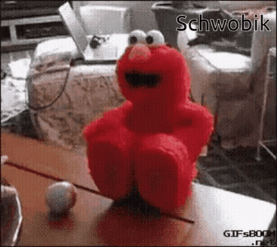 Elmo From Sesame Street Is Sitting On A Table With A Ball GIF