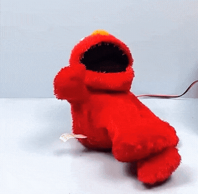 elmo from sesame street is sitting on a table with his mouth open and looking at the camera .