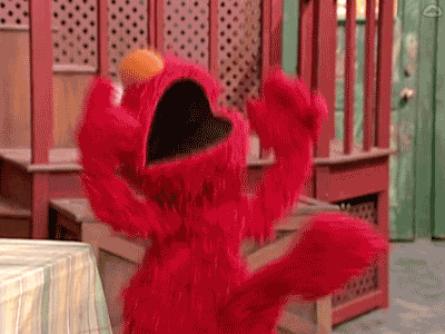 Elmo From Sesame Street Is Standing In Front Of A Table With His Mouth Open And His Arms Outstretched . GIF