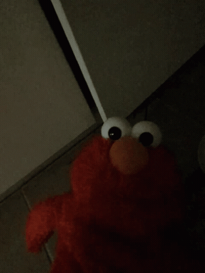 Elmo From Sesame Street Is Standing In The Corner Of A Dark Room GIF