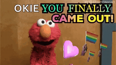 Elmo From Sesame Street Says " Okie You Finally Came Out " While Holding A Heart And Rainbow Flags GIF