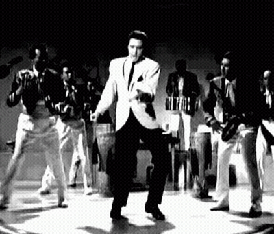 Elvis Presley Is Dancing On A Stage In A Black And White Photo With A Band Behind Him . GIF