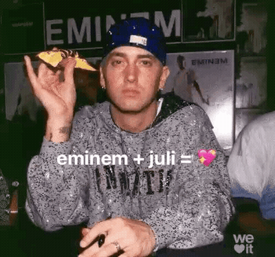 Eminem Is Holding A Piece Of Pizza In His Hand While Wearing A Blue Hat . GIF