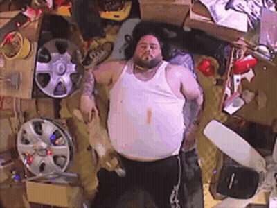 Fat Man Laying On Bed Surrounded By Wheels And Boxes GIF