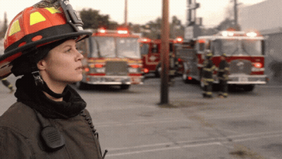 Female Firefighter With Helmet And Walkie Talkie In Front Of Fire Trucks GIF