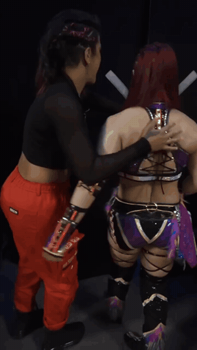 Female Wrestler Standing Next To Wrestler In Red Pants With X On Pocket GIF