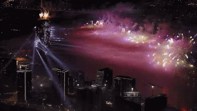 Fireworks Are Displayed Over A City With A Purple Sky In The Background GIF