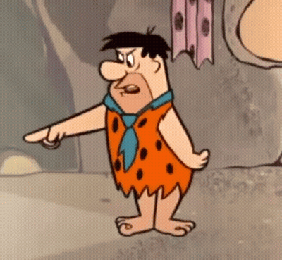 Flintstone From The Flintstones Is Standing In Front Of A Rock Wall And Pointing At Something . GIF