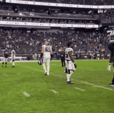Football Player In Jersey Number 65 Walking On Field GIF