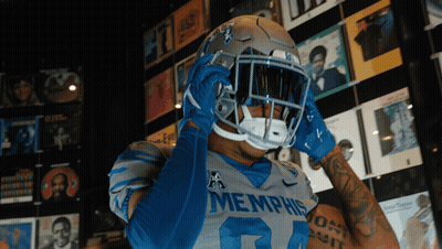 Football Player In Memphis Jersey And Helmet In Front Of CD Wall GIF