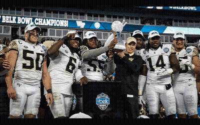 Football Players Holding Trophy In Front Of Belk Bowl Sign GIF