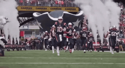 Football Players Running On Field With Smoke From Tunnel GIF