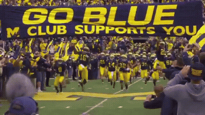 Football Team Running With Go Blue M Club Banner