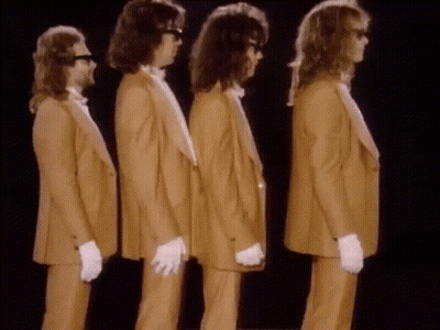 Four Men In Tan Suits And White Gloves Are Standing In A Row GIF