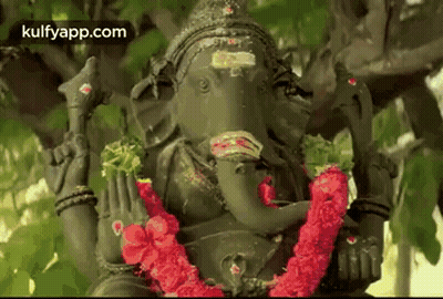 Ganesha Statue Sitting Under Tree With Red Flower Garland GIF