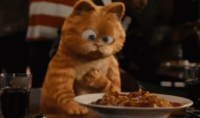 Garfield The Cat Is Sitting At A Table With A Plate Of Food GIF
