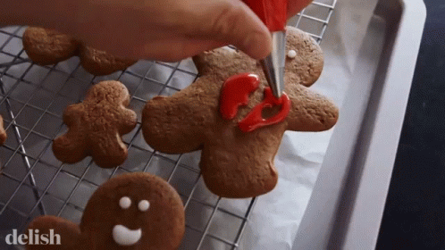 Gingerbread Men Are Being Decorated With Red Frosting And The Word Delish Is In The Corner GIF